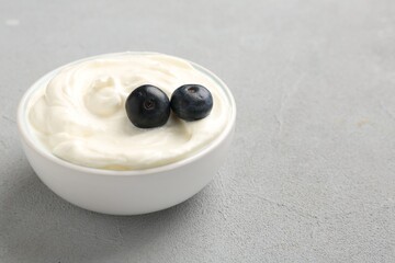 Delicious yogurt with blueberries in bowl on grey table, closeup. Space for text