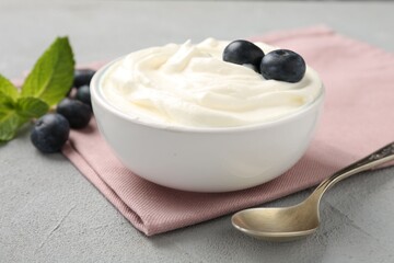 Delicious yogurt in bowl, blueberries, mint and spoon on grey table, closeup