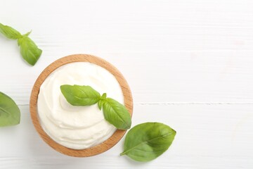 Delicious yogurt in bowl and basil on white wooden table, flat lay. Space for text