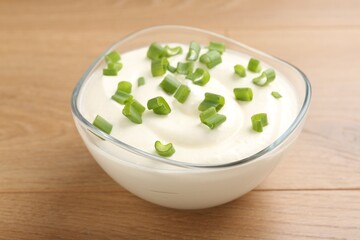 Delicious yogurt with green onions in bowl on wooden table, closeup