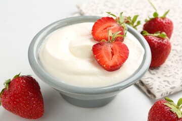 Delicious yogurt in bowl and strawberries on white table, closeup