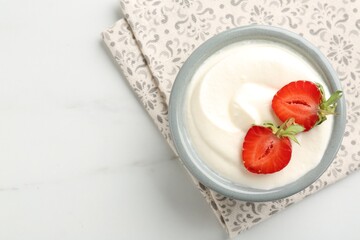Delicious yogurt in bowl and strawberries on white marble table, top view. Space for text