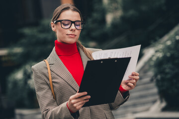 Confident businesswoman reviewing documents outdoors in a stylish city setting for professional and...