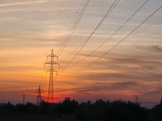 High voltage pylon and power lines silhouetted against a dramatic fiery sunrise sky. Stunning contrast of technology and nature.