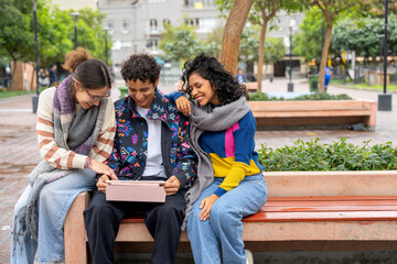 Young students sharing a digital tablet on a city bench