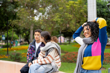 Young latin woman fixing her hair while walking in a park with friends