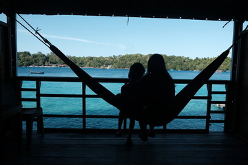Serene Silhouette: Mother and Child Relaxing in Hammock Overlooking Tropical Waters
