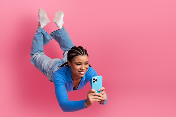 Cheerful young woman enjoying leisure time scrolling on phone against a vibrant pink background in...
