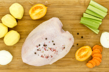Raw chicken breast with skin and raw vegetables, for boiling, cooking, baking on a wooden cutting...