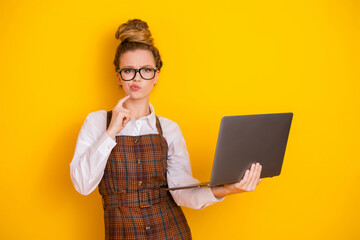 Teen girl woman in a striped apron holding a laptop, standing before a bright yellow background