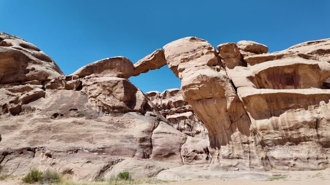 Breathtaking view of the iconic Um Fruth rock bridge, showcasing the natural arch and towering sandstone formations under a clear blue sky in Jordan's Wadi Rum desert