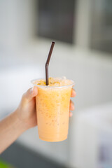 hand of woman holding a take-out iced thai tea latte at cafe, isolate concept.