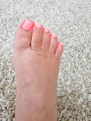 Female Foot with Pink Toenail Polish on a White Carpet 
