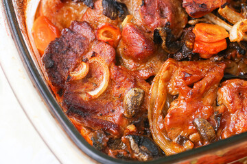 Traditional baked meat dish. Juicy pork with vegetables in glass baking dish. Home cooked dinner rustic presentation. Roasted onions, carrots, mushrooms. Tasty homemade meal. Oven cooked comfort food