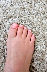 Female Foot with Pink Toenail Polish on a White Carpet 