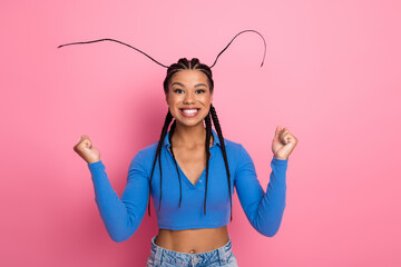 Joyful young woman with styled braids smiling confidently in casual blue top and jeans against a...