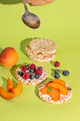 Rice cakes with different types garnish fruits, peaches, blueberries, apricots, raspberries with honey on green background. Healthy colorful food.