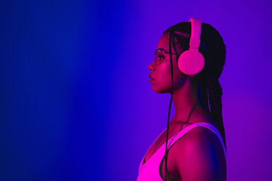 Profile view of a stylish young woman in vibrant neon lighting wearing headphones, representing creative individuality and modern fashion. - Powered by Adobe