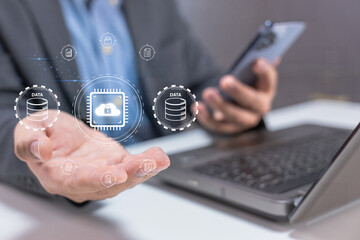 A person holds a smartphone near a laptop, with digital icons symbolizing data security and encryption floating above the open hand.