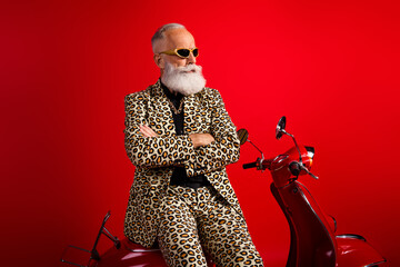 Stylish elderly gentleman in leopard print suit and sunglass posing confidently on scooter against...