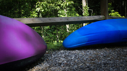 colorful kayaks propped up against a split rail fence with trees in the background. recreation and...