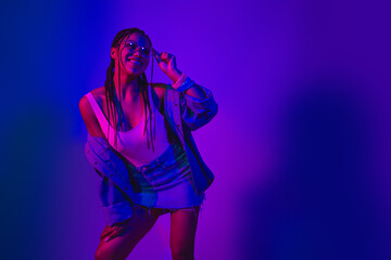 Young woman enjoying vibrant mood in a neon-lit setting with stylish denim outfit showing joy and...