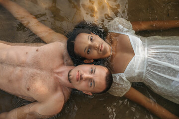 Romantic interracial couple lying in water, heads touching, serene and intimate moment, love,...