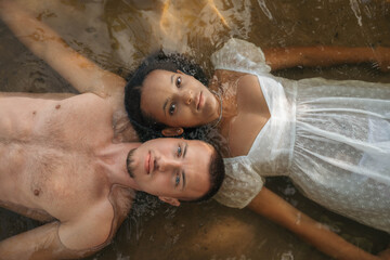Romantic interracial couple lying in water, heads touching, serene and intimate moment, love,...