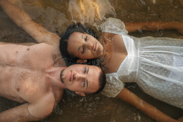 Romantic interracial couple lying in water, heads touching, serene and intimate moment, love,...