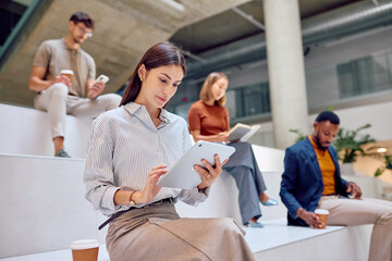 Businesswoman using digital tablet in modern office lobby, colleagues reading and using smartphone in background