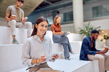 Portrait of a smiling businesswoman using digital tablet with colleagues in background in modern office building