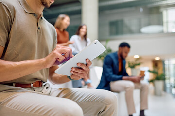 Close up of male hands using digital tablet in office lobby, with blurred colleagues in background