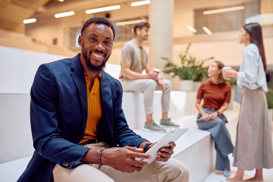 Portrait of a smiling businessman using a tablet in a modern office lobby with his colleagues chatting in the background