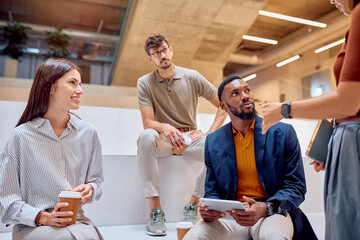 Diverse colleagues gathering in modern office lobby and discussing new project during coffee break