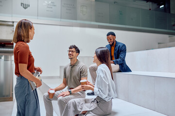 Four young professionals chatting and enjoying coffee during a break in a modern office space,...