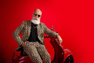 Charismatic elderly man in a leopard print suit posing confidently on a red scooter against a...