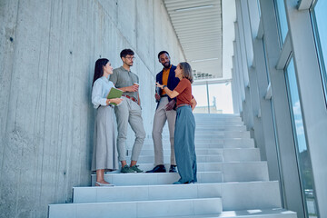 Multi-ethnic businesspeople talking and having coffee break on stairs in modern office building