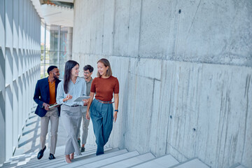 Group of multi-ethnic businesspeople walking up stairs in modern office building while discussing...