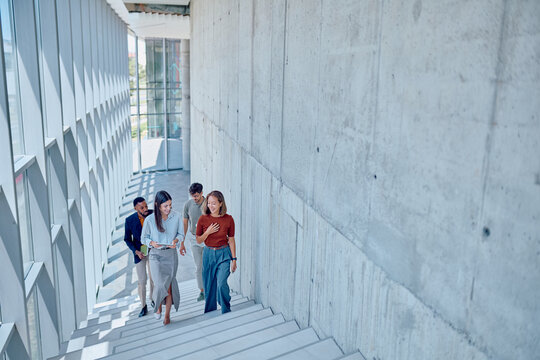 Group of happy businesspeople walking and talking while going down the stairs in a modern office building