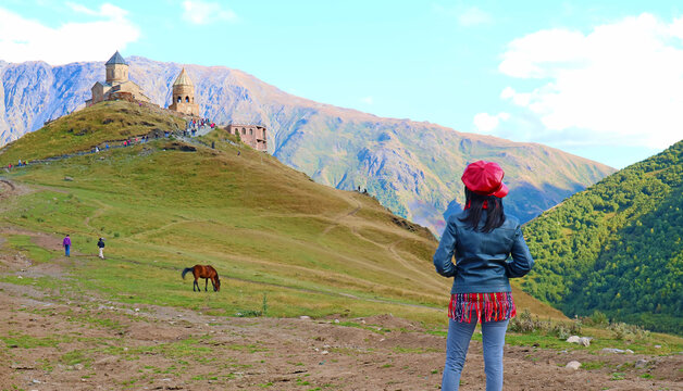 Visitor Enjoying the Iconic View of Medieval Gergeti Trinity Church with Kazbek Mountain in the Backdrop, Stepantsminda, Georgia