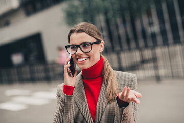 Professional businesswoman in formal attire speaking on cellphone outdoors in a vibrant urban...