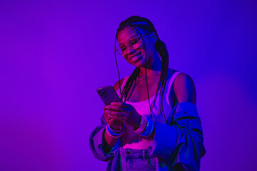 Young woman using mobile phone in neon lighting with a stylish denim outfit creating a modern vibrant atmosphere