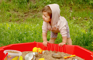 little girl in a hoodie standing by the sandbox