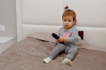 little girl trying to use tv remote control sitting on bed