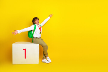 Cheerful young boy celebrating success with a medal against a vibrant yellow background,...