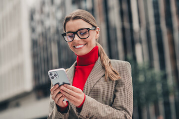 Stylish professional in elegant attire checking her phone outdoors in urban city against modern...