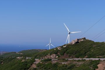 Wind turbines that rise in the green coastal hill, generating renewable electricity, electric lines that extend through the blue horizon and an expansive marine landscape