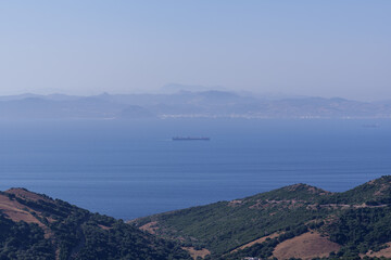 Cargo vessel navigating narrow gibraltar strait, connecting european and african coastlines, symbolizing international maritime commerce