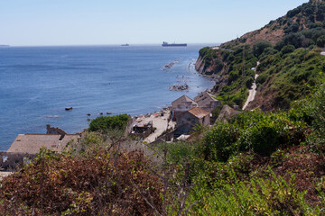 Cargo ships navigating the strait of gibraltar with an abandoned coastal mining village in the foreground