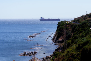 Cargo ship navigating on blue sea with rocky coastline and electricity infrastructure